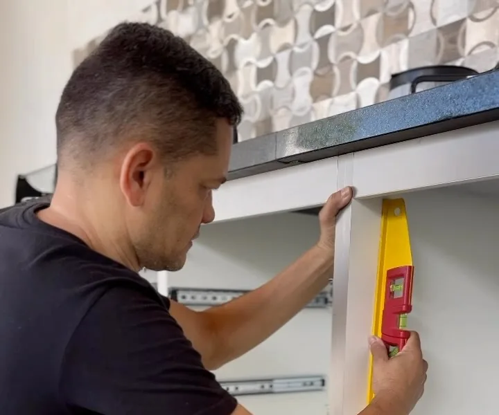 Juafran conferindo o nível de um armário de cozinha durante a montagem